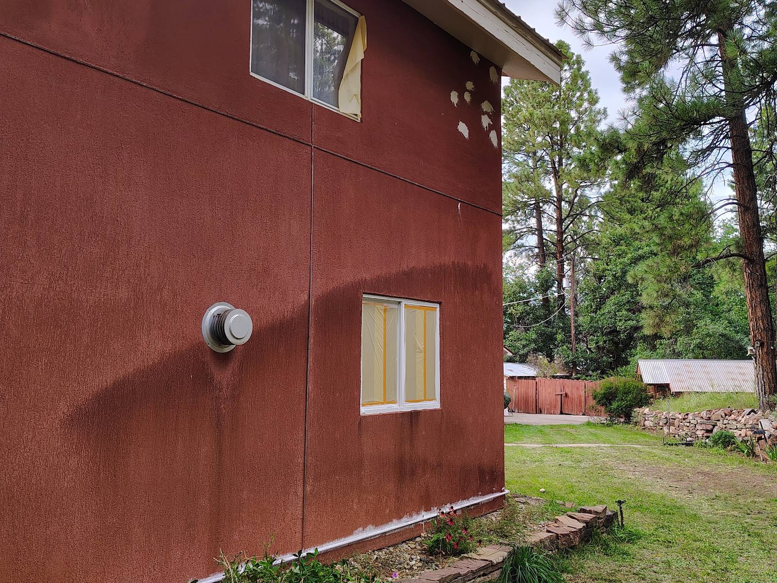 Two-story cottage in red stucco with patched woodpecker holes across the wall