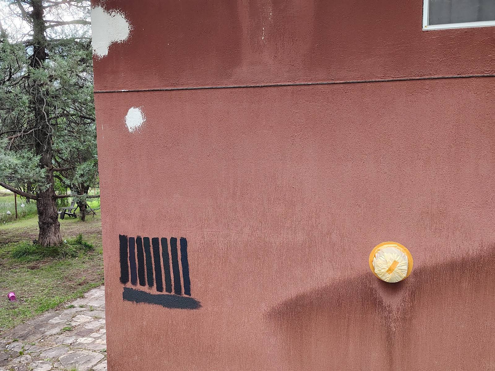 Patched woodpecker holes and masked fittings on the red stucco wall before painting
