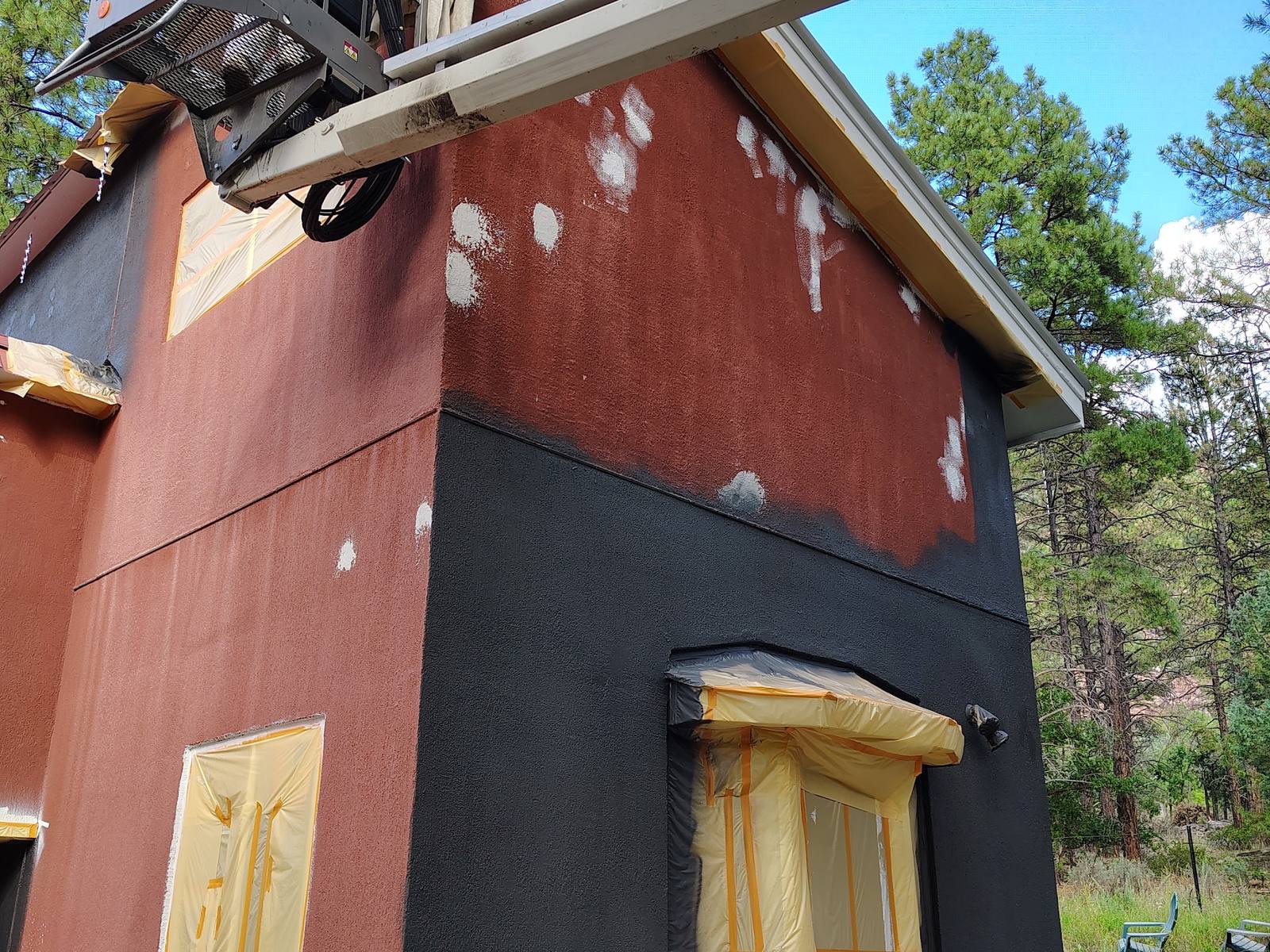 The cottage half repainted, red stucco above and charcoal below, with a lift in the yard