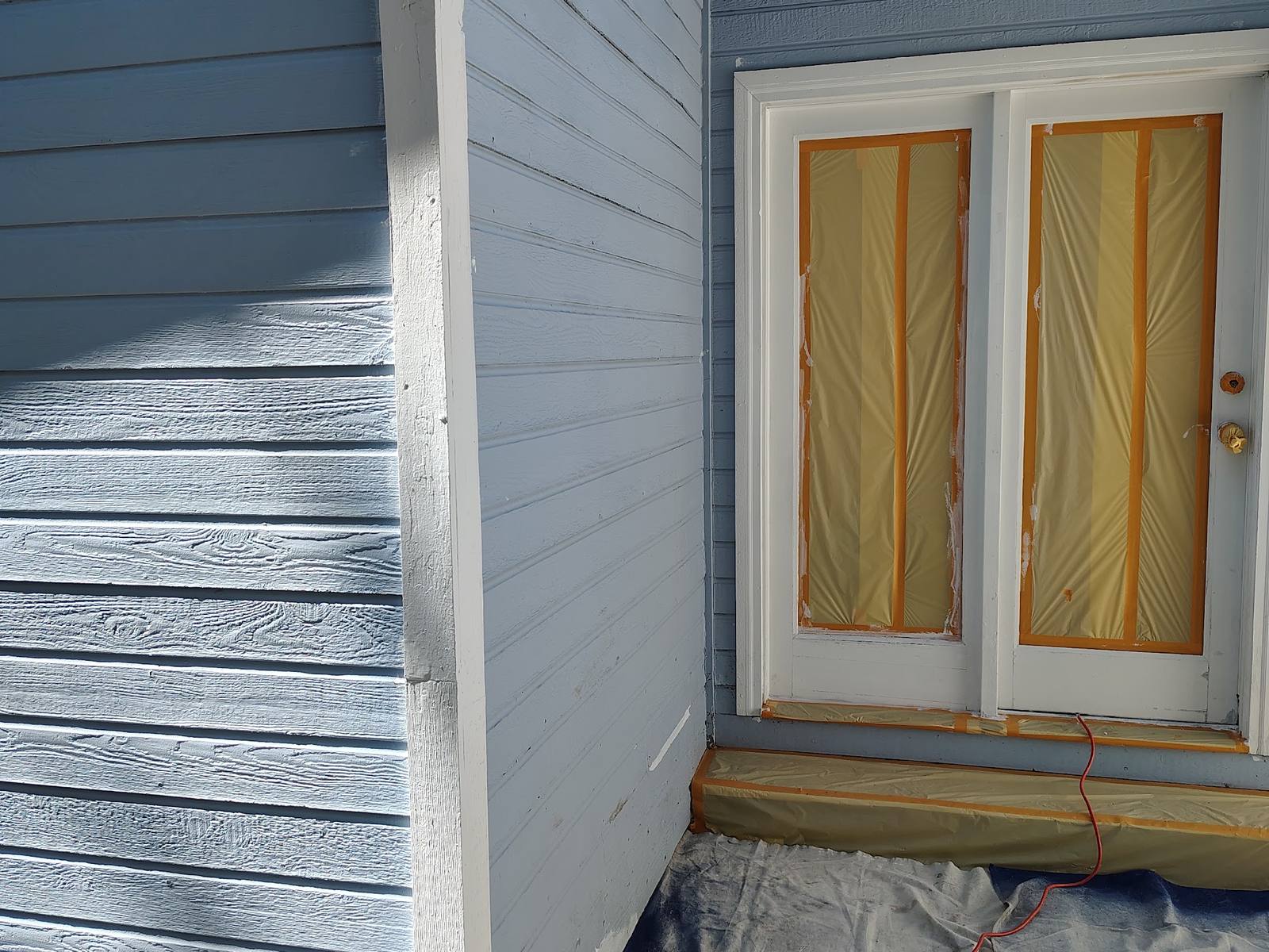 Pale weathered lap siding and a masked door before painting